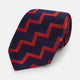 The Turnbull & Asser UK Seven-Fold Silk Red and Navy Geometric Tie is displayed rolled with its tip forward, showcasing its bold navy and red geometric pattern against a plain white background.