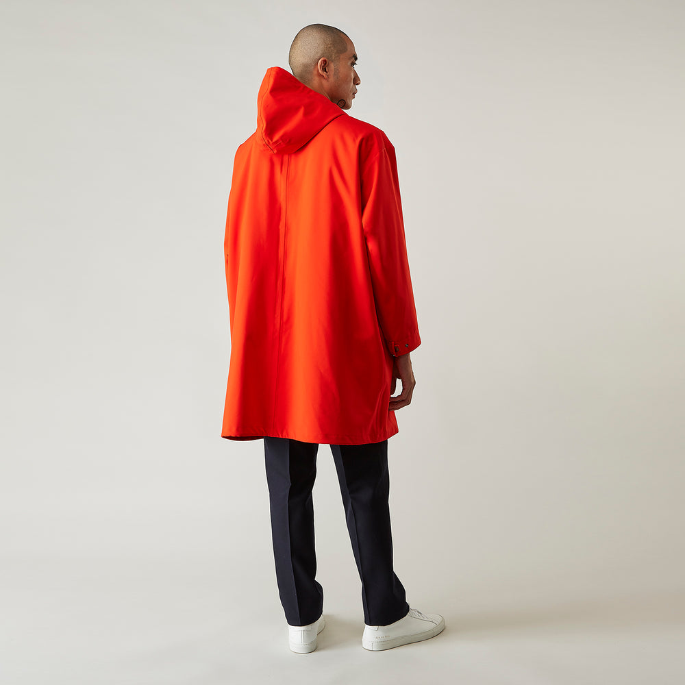 Wearing the Turnbull & Asser Red Walter Sealup Parka with Detachable Liner, black pants, and white sneakers, a person stands in profile against a plain light background—perfect for travel.