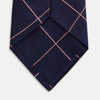 View 4 of product The Turnbull & Asser FONDANT PINK and WINDOW PANE NAVY Silk Tie features a subtle ribbed texture with a pink grid pattern on navy—an elegant choice for polished office attire, shown neatly rolled on a white background.