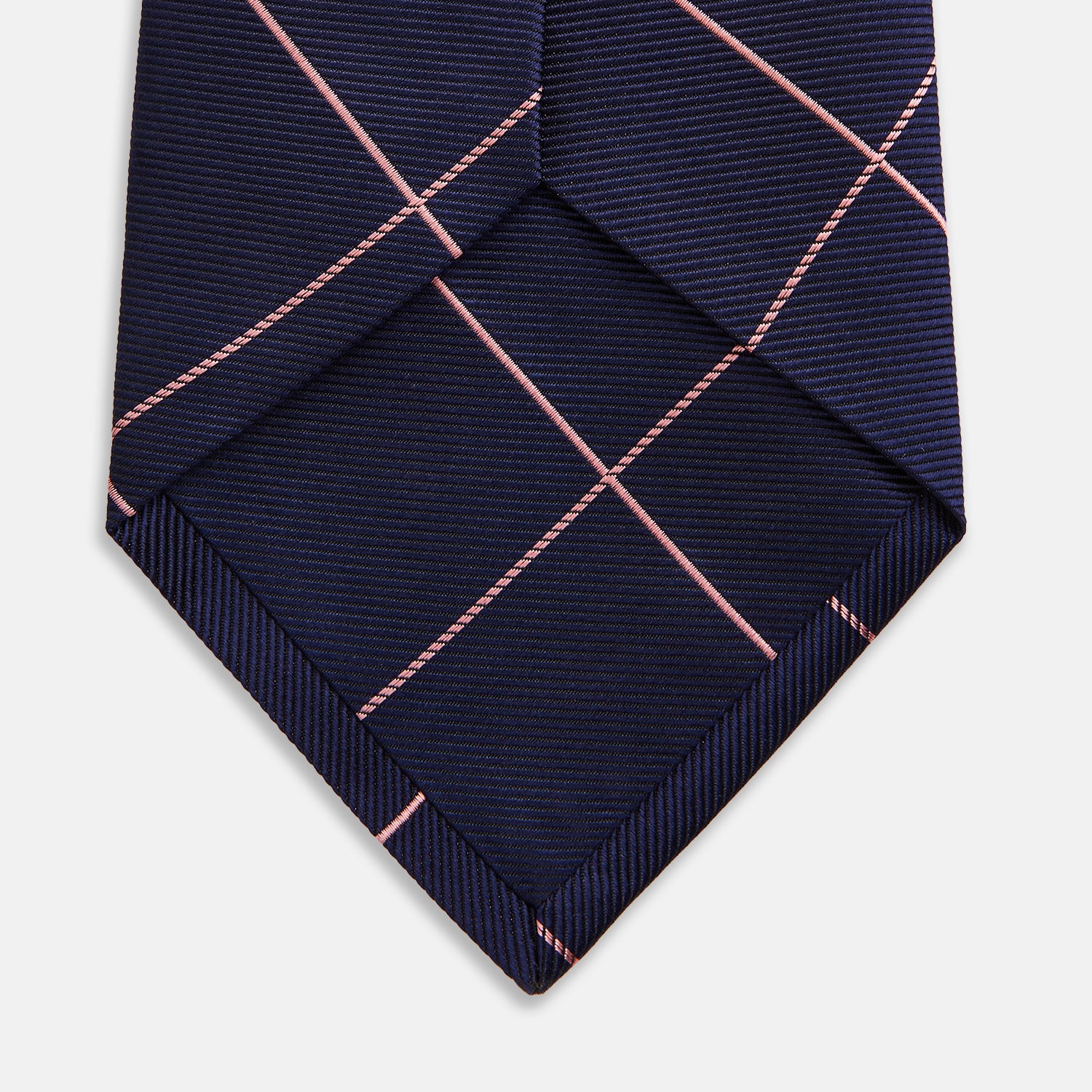 View 4 of product The Turnbull & Asser FONDANT PINK and WINDOW PANE NAVY Silk Tie features a subtle ribbed texture with a pink grid pattern on navy—an elegant choice for polished office attire, shown neatly rolled on a white background.