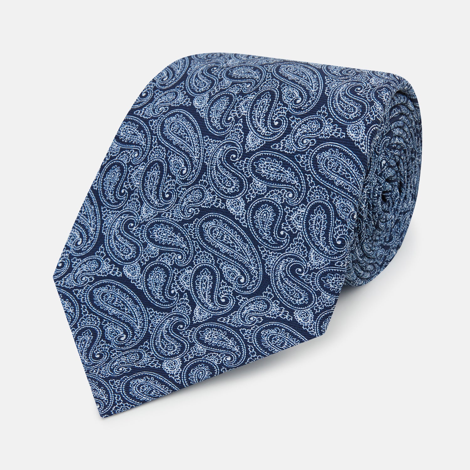 View 1 of product The Turnbull & Asser Dark Navy Paisley Silk Tie, featuring a detailed white paisley pattern, is neatly rolled and displayed against a plain white background.