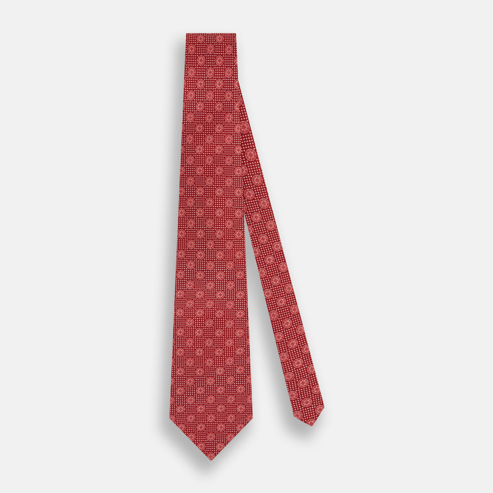 The Turnbull & Asser Red Medallion Silk Tie features a rolled-up red silk design with a repeating geometric pattern of small white circles and cross motifs on a plain white background.