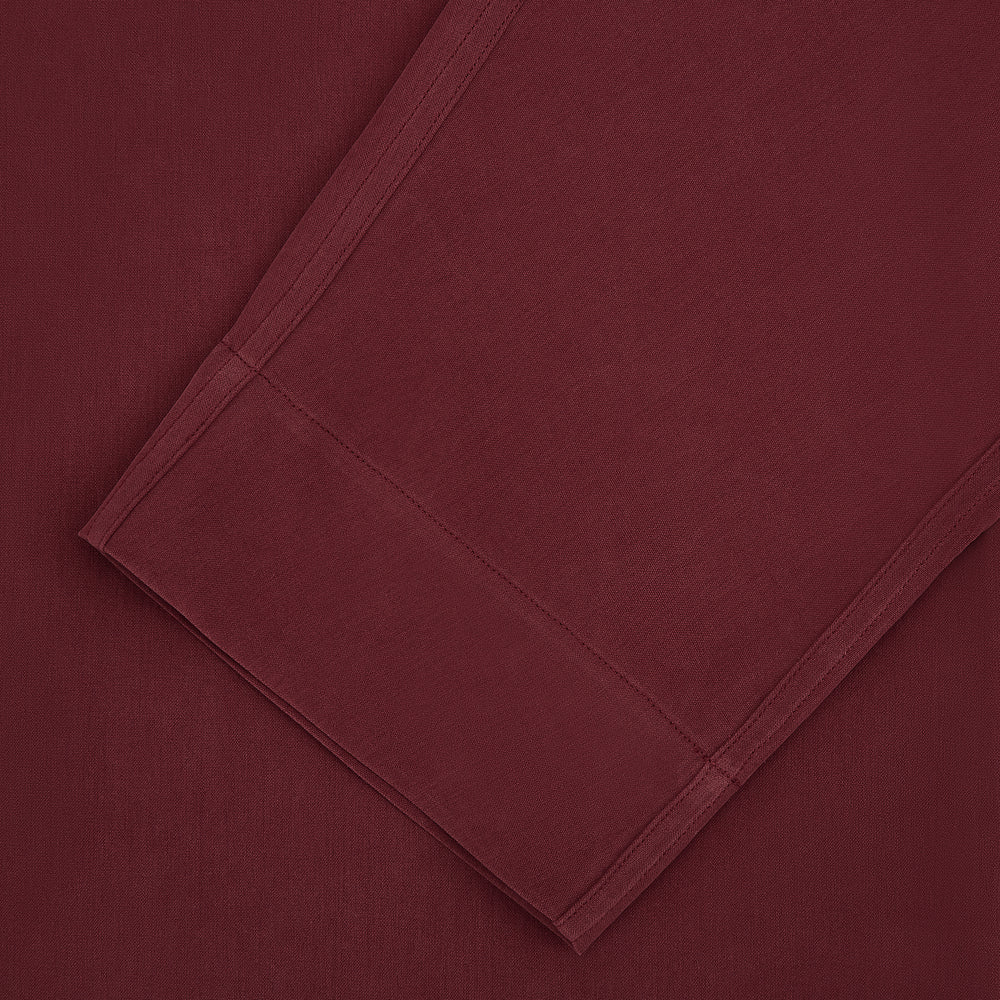 The Turnbull & Asser Burgundy Silk Pyjama Set features a long-sleeve, button-up shirt with chest pocket and matching pants with elastic waistband and side pocket, shown on a white background.