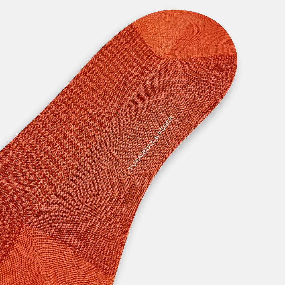 The Orange Houndstooth Mid-Length Socks by Turnbull & Asser feature a bold houndstooth pattern with solid orange toe, heel, and cuff, crafted from soft cotton and shown against a plain white background.