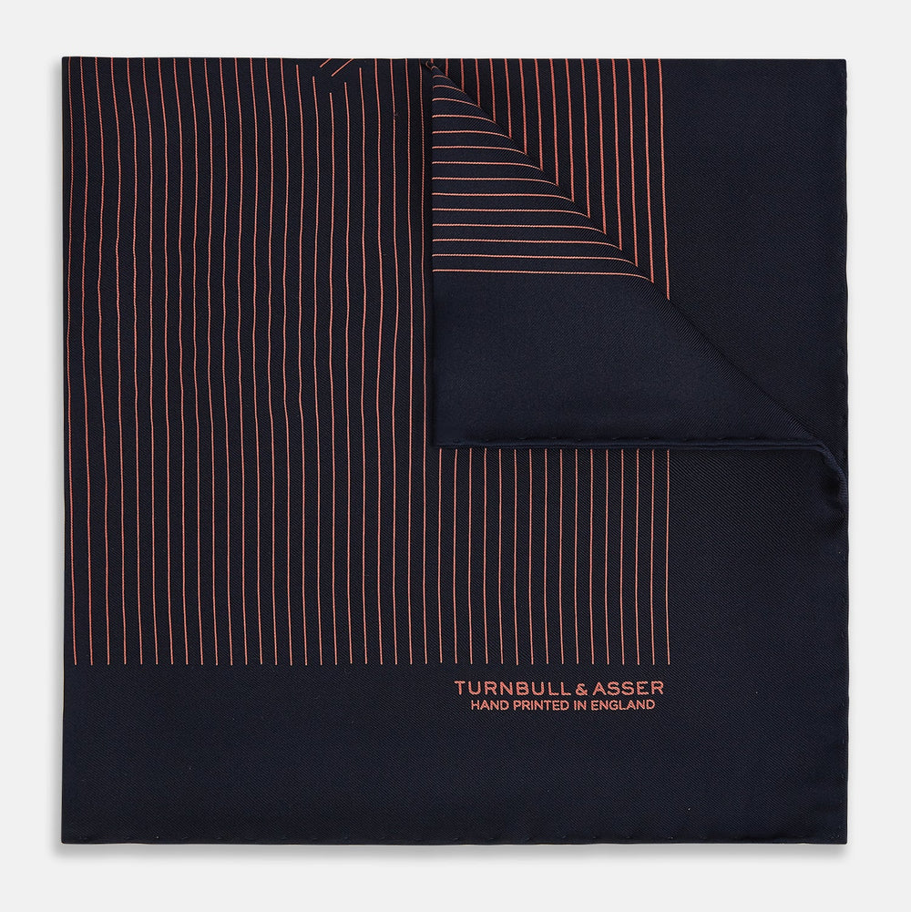 The Navy and Orange Stripe Silk Pocket Square by Turnbull & Asser is handmade in England from silk, featuring thin orange geometric stripes on navy and "Turnbull & Asser Hand Printed in England" printed in the corner.