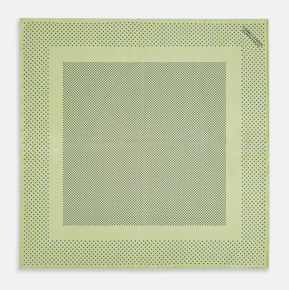 The Melon Green Dot Silk Pocket Square by Turnbull & Asser is handmade in England from silk, featuring small black polka dots. Shown folded with a turned-up corner, it displays both sides of the light green fabric.