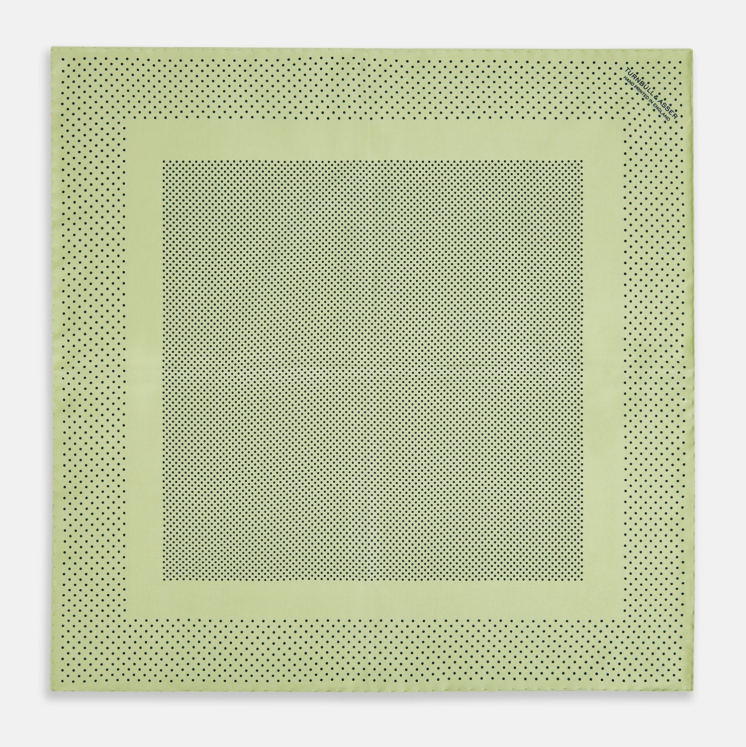 View 4 of product The Melon Green Dot Silk Pocket Square by Turnbull & Asser is handmade in England from silk, featuring small black polka dots. Shown folded with a turned-up corner, it displays both sides of the light green fabric.