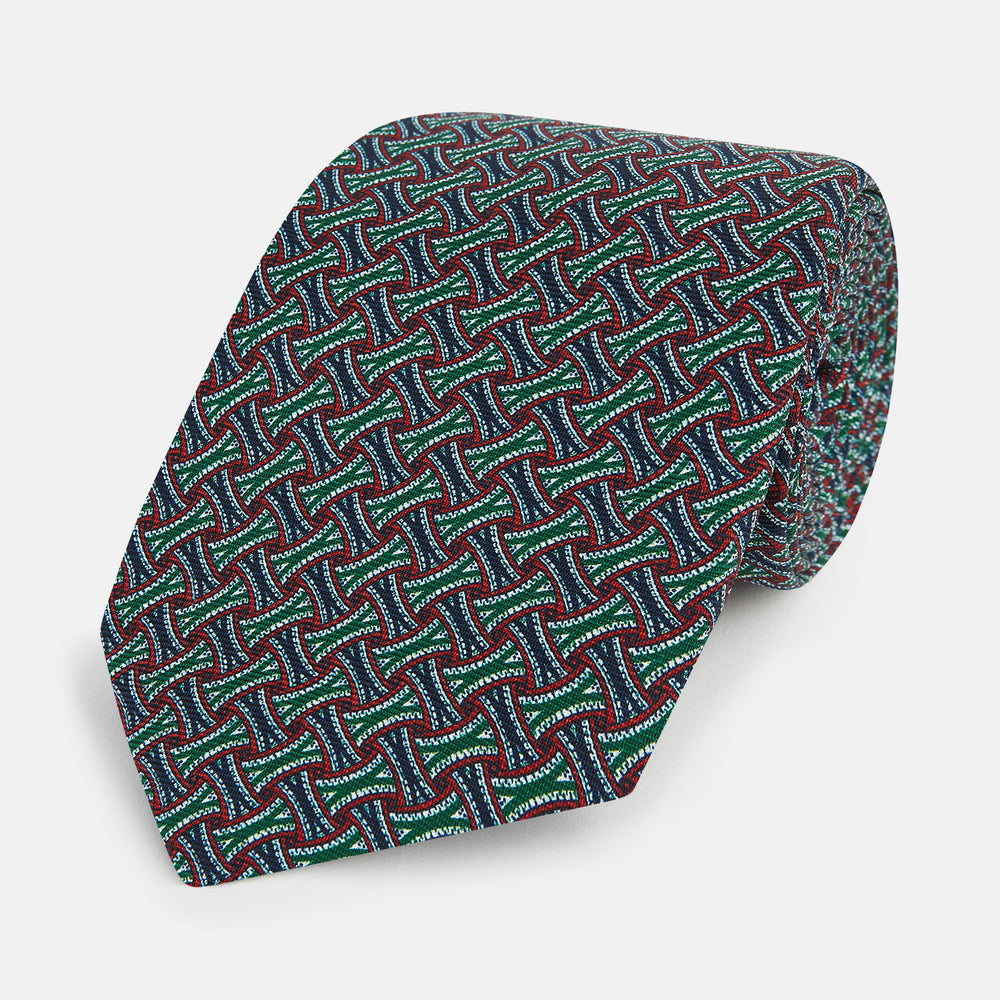 The Forest Green and Red Weave Patterned Silk Tie by Turnbull & Asser features a geometric interlocking design in red, blue, and green, elegantly rolled on a white background.