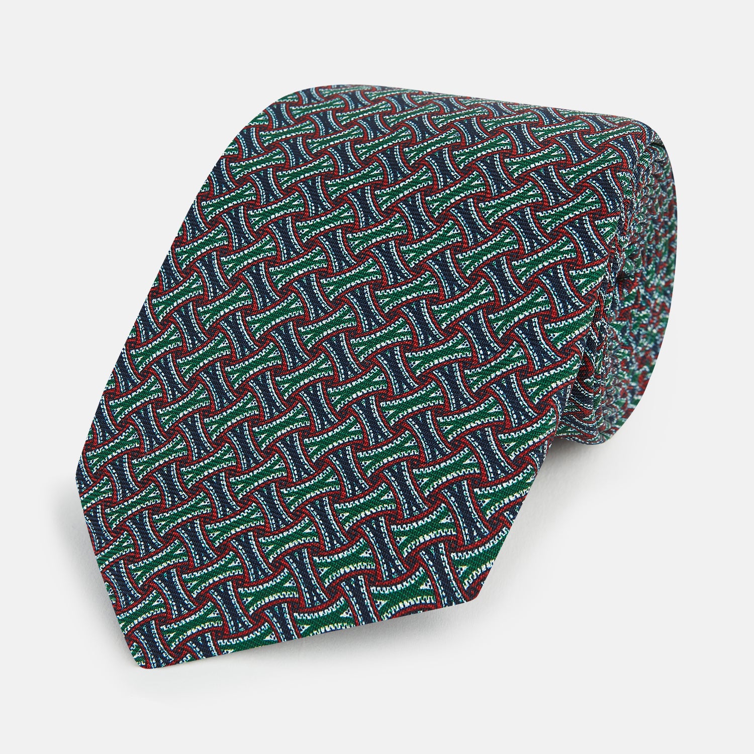 View 1 of product The Forest Green and Red Weave Patterned Silk Tie by Turnbull & Asser features a geometric interlocking design in red, blue, and green, elegantly rolled on a white background.