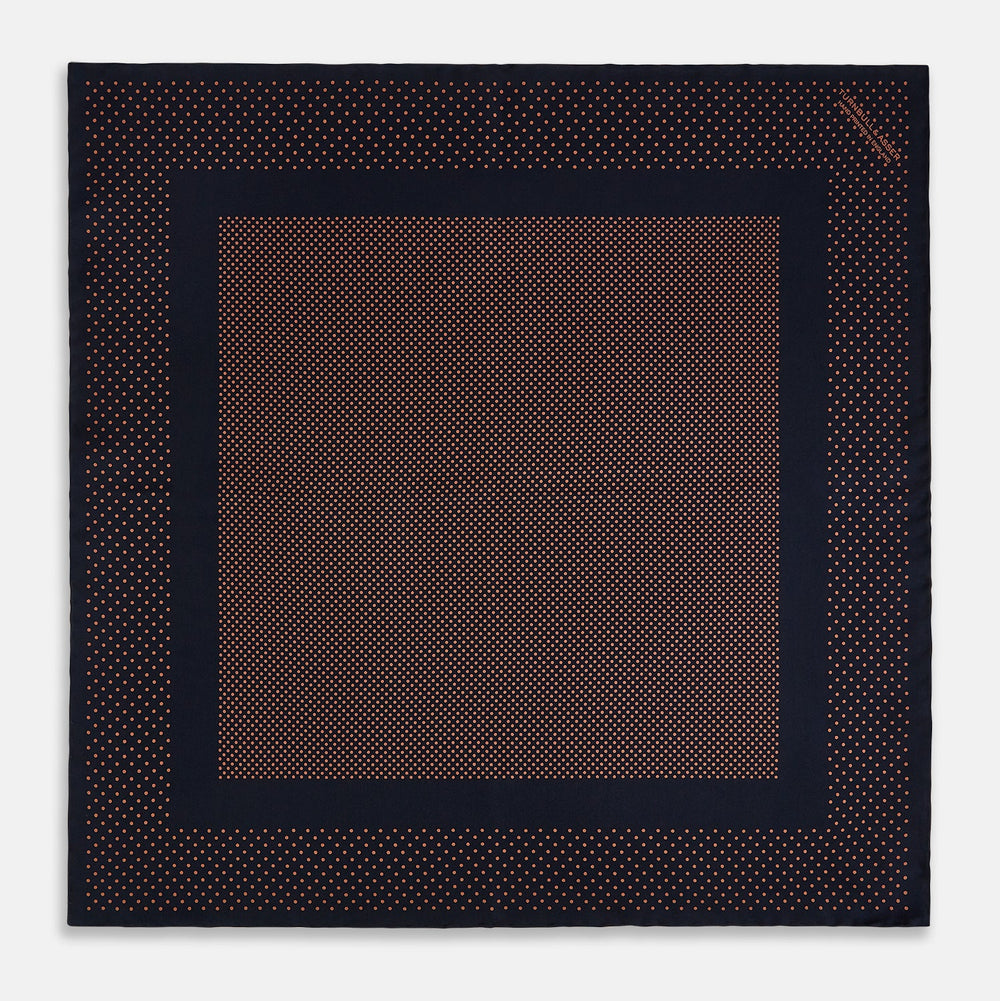 The Navy and Blush Dot Silk Pocket Square by Turnbull & Asser features a navy base with small orange polka dots and a border, shown neatly folded with one corner flipped over.