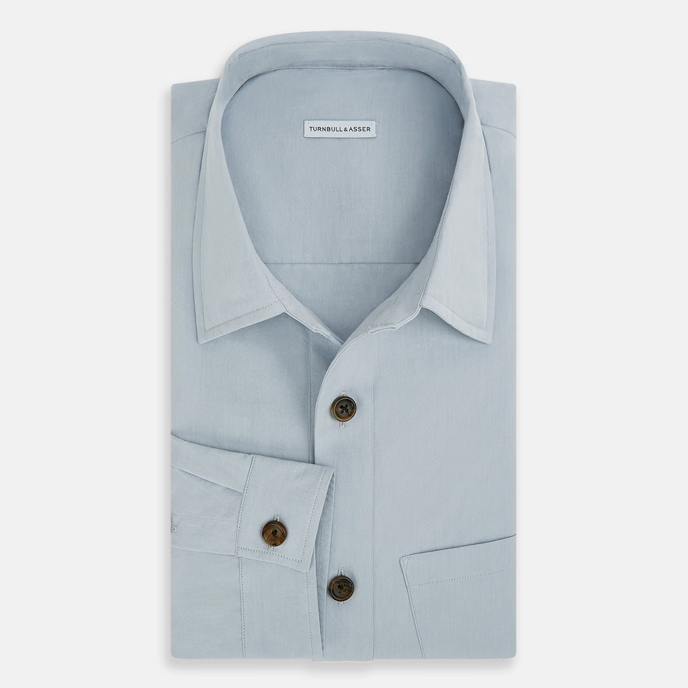 The Turnbull & Asser Grey Hyde Overshirt is a long-sleeve button-up made from sanforised cotton, featuring a single chest pocket and dark buttons, shown against a plain white background.