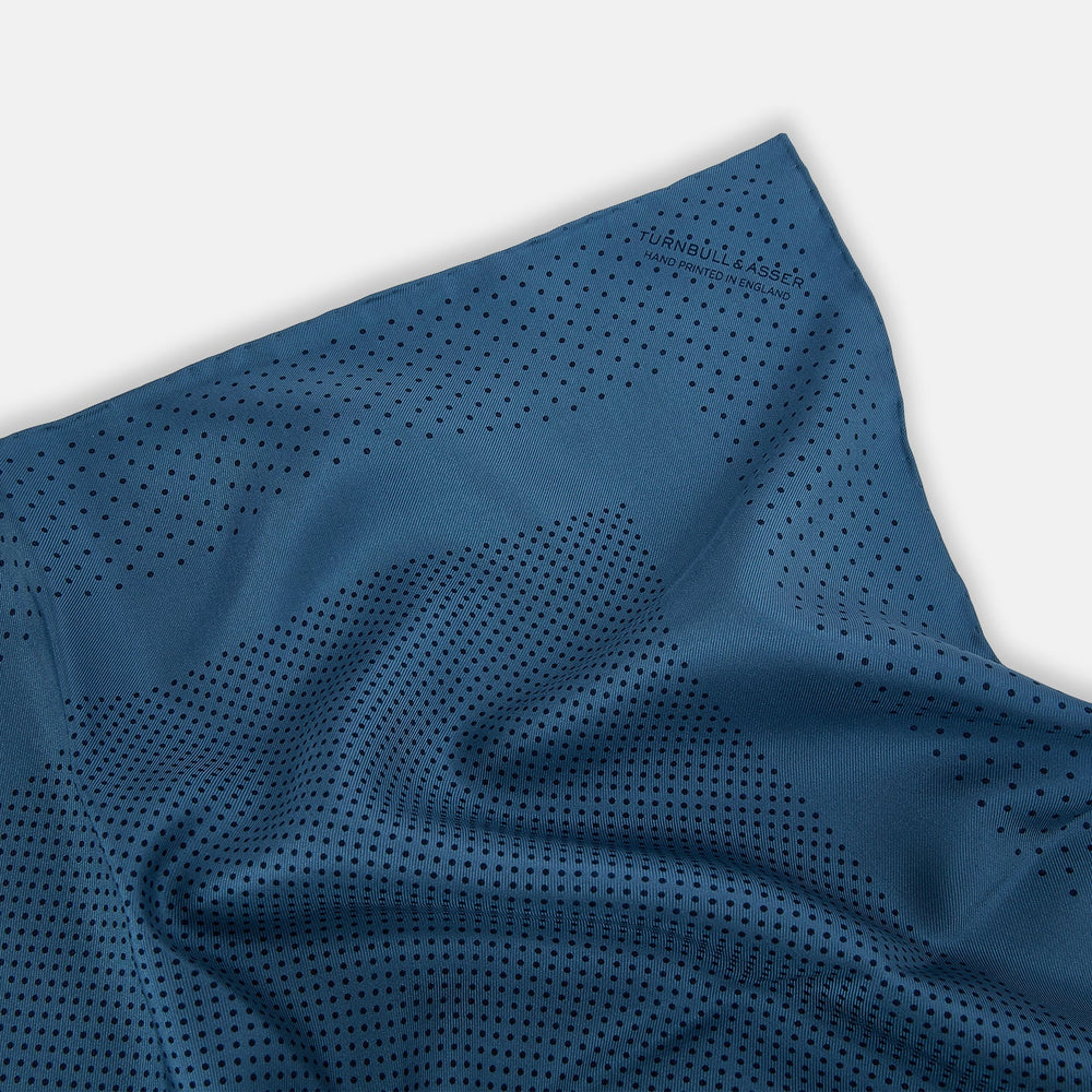 The Blue Dot Silk Pocket Square by Turnbull & Asser features small black polka dots on blue silk and is made in England. The image shows it neatly folded, with a corner turned down to display both sides.