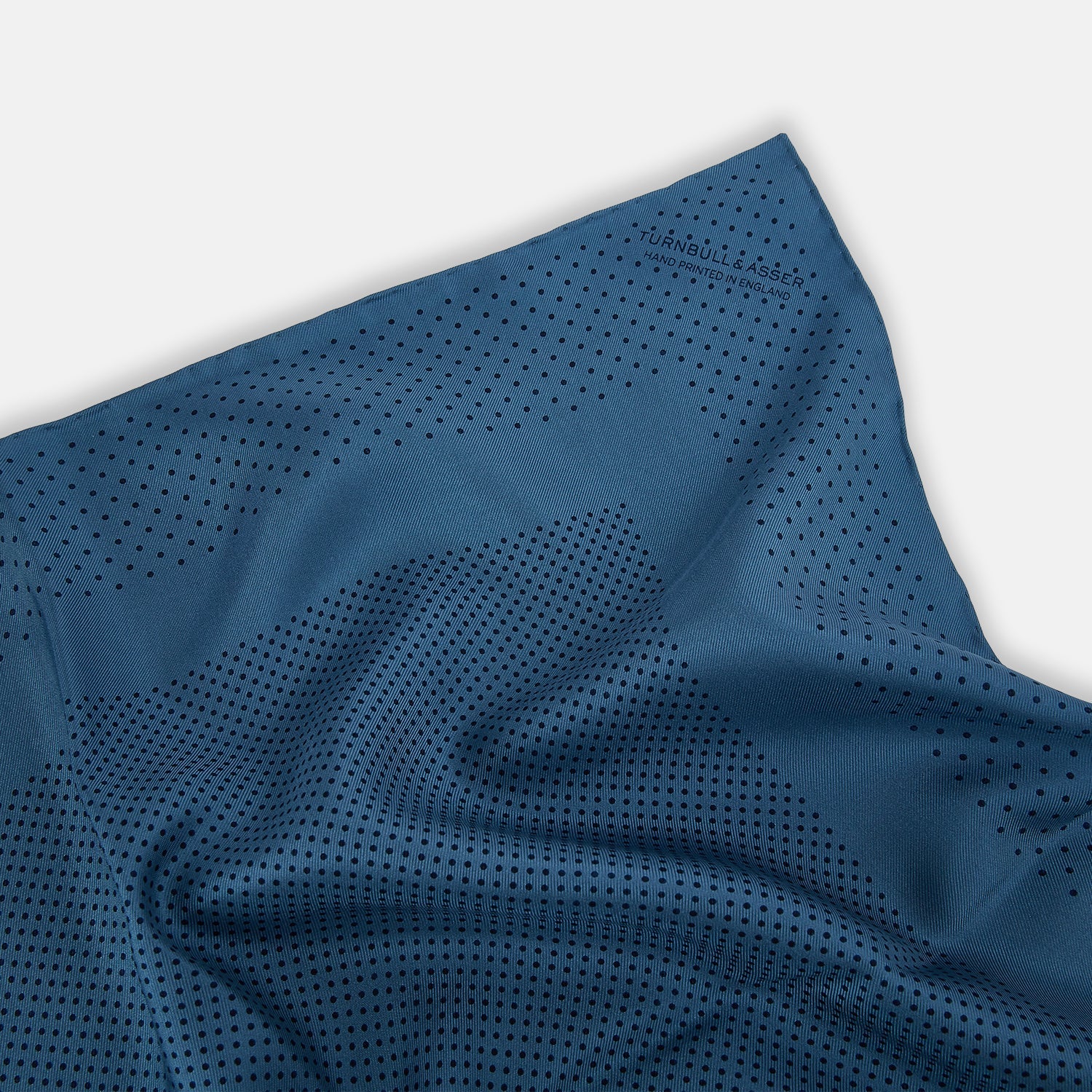 View 2 of product The Blue Dot Silk Pocket Square by Turnbull & Asser features small black polka dots on blue silk and is made in England. The image shows it neatly folded, with a corner turned down to display both sides.