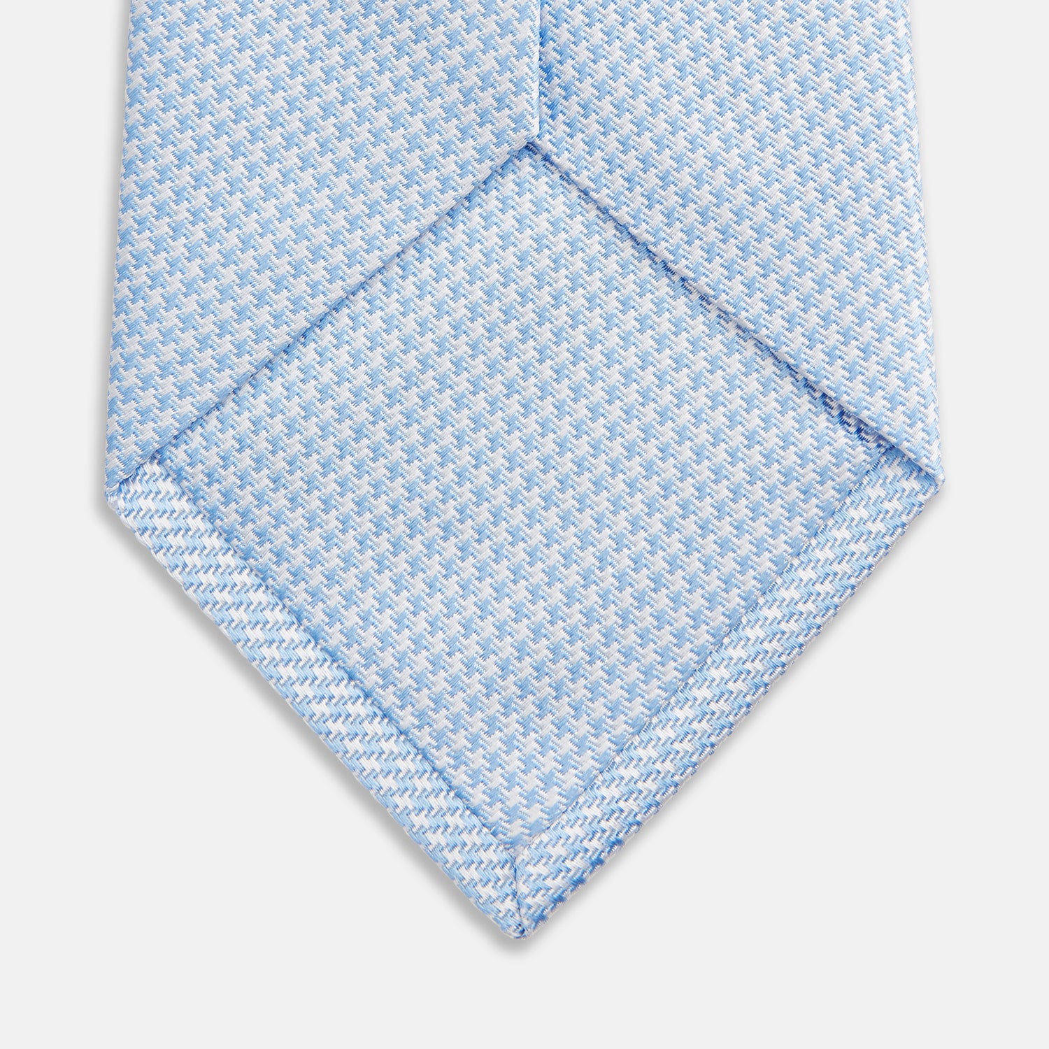 View 3 of product The HOUNDSTOOTH WHITE RIVER TIE by Turnbull & Asser features a light blue and white textured pattern, making it an essential accessory for elegant looks, shown beautifully rolled on a plain white background.