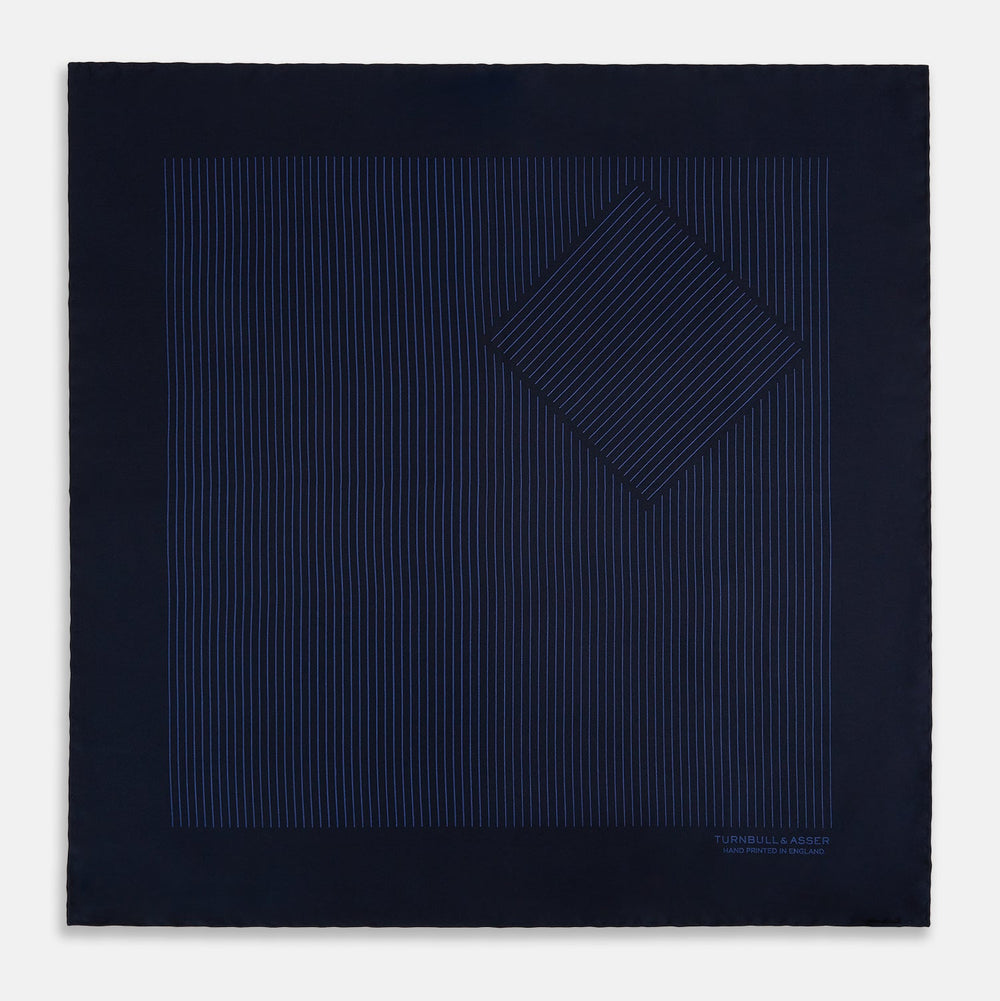 The Navy Stripe Silk Pocket Square by Turnbull & Asser features a dark navy silk with thin light blue stripes and hand-rolled edges, folded to reveal both sides and “TURNBULL & ASSER HAND PRINTED IN ENGLAND” in the corner.