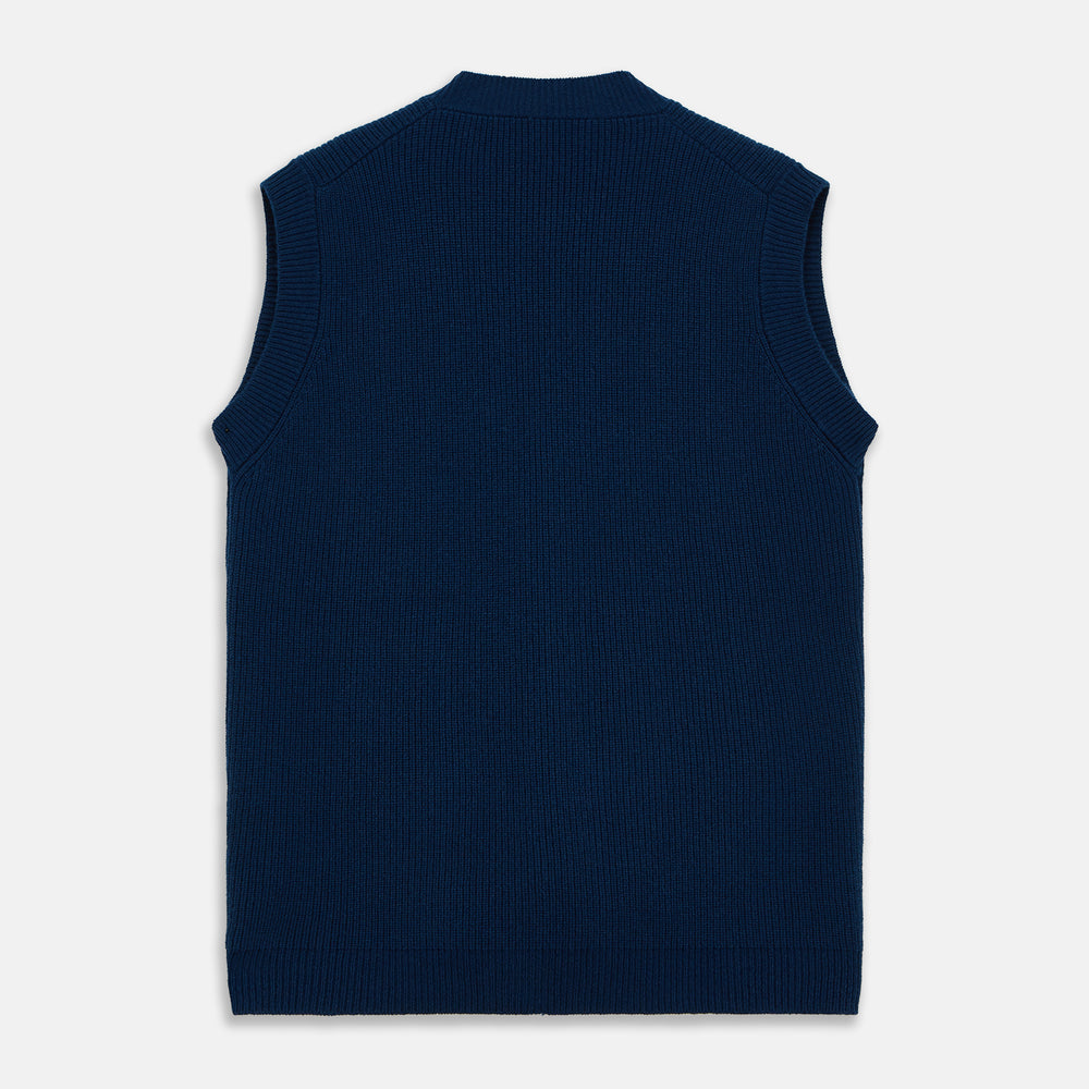 A man with a shaved head wears a Turnbull & Asser Navy Sleeveless Cashmere Cardigan over a white dress shirt with rolled-up sleeves and dark trousers, standing against a plain light gray background.