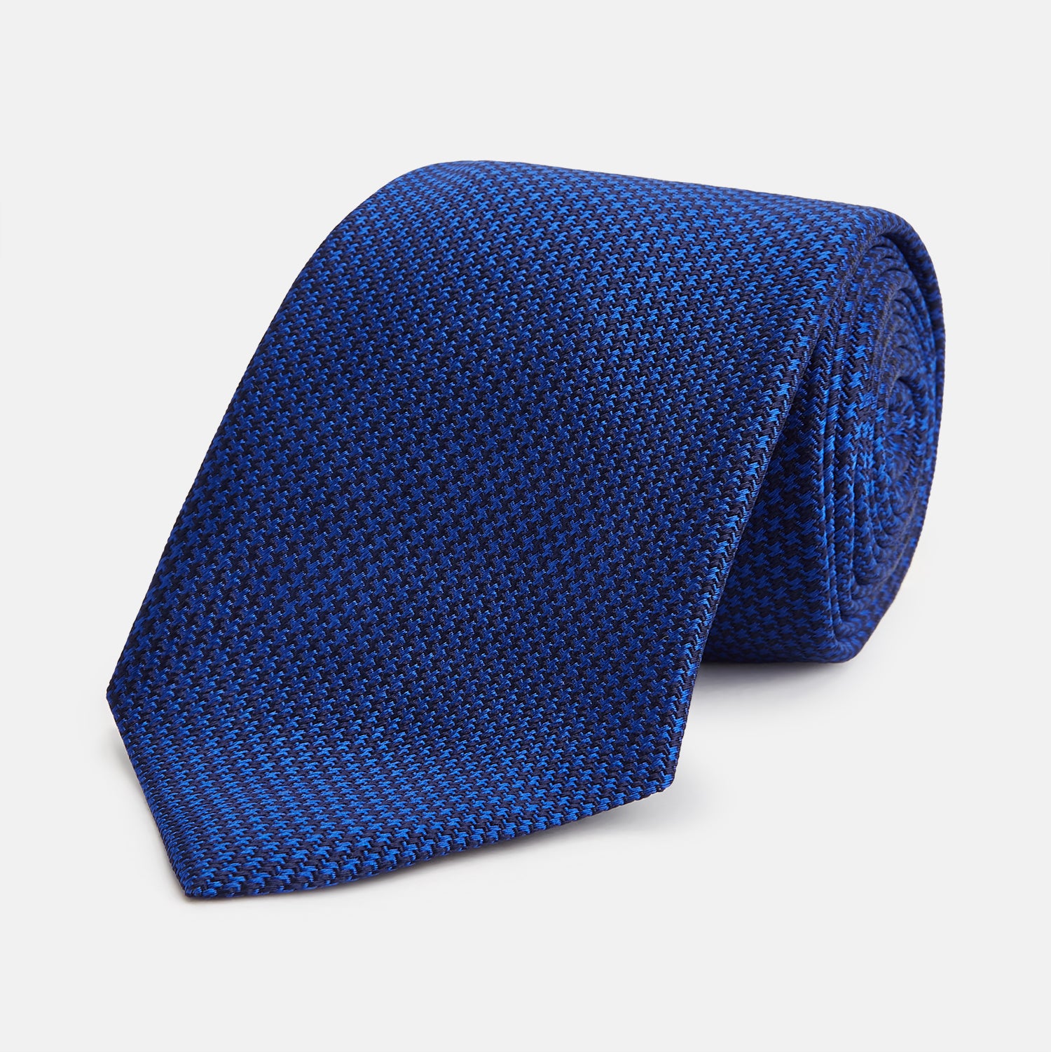 View 1 of product The HOUNDSTOOTH NAVY CRUISE TIE by Turnbull & Asser, featuring a textured blue design, is displayed rolled-up on a plain white background—an essential accessory for elevating formal looks.