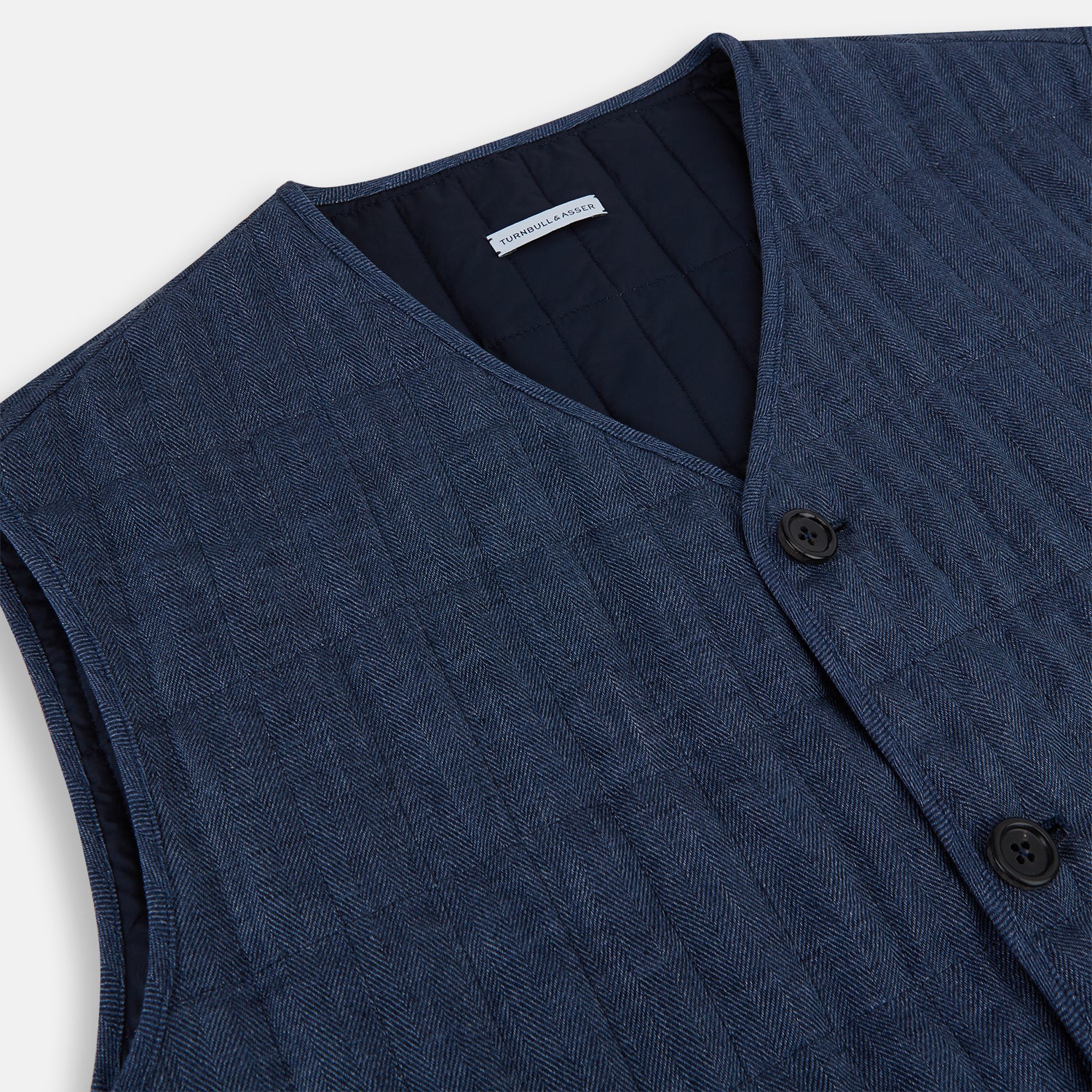View 2 of product The Denim Blue Quilted Linen Herringbone Waistcoat by Turnbull & Asser features a sleeveless design, five black buttons, two zippered side pockets, and a small chest pocket against a plain white background.