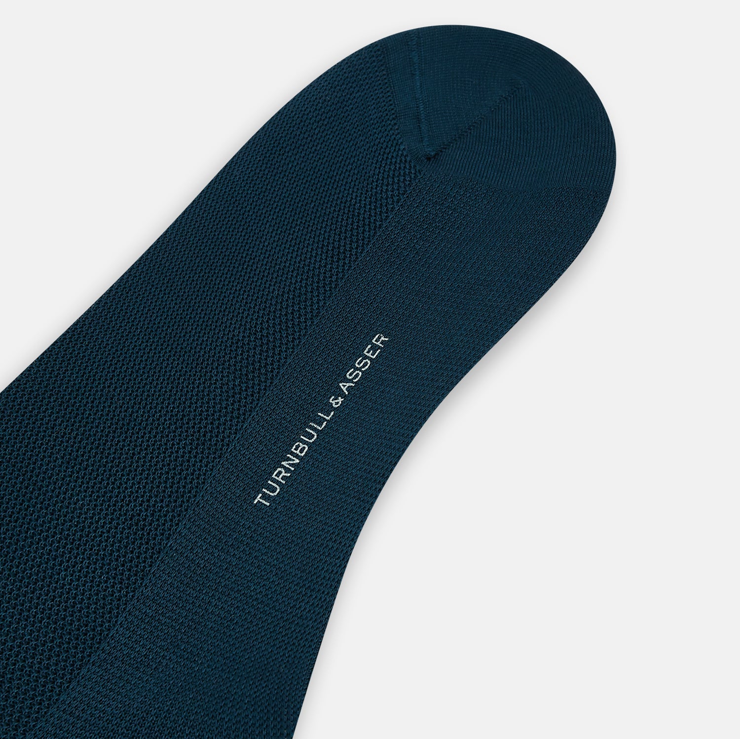 View 3 of product The Turnbull & Asser Petrol Micro Knit Long Sock, shown in dark blue and over the calf length, is displayed on a white background angled to display its full length from toe to cuff.