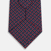 View 3 of product The Turnbull & Asser Navy and Pink Woven Printed Silk Tie features a geometric pattern with interlocking lines, displayed rolled on a light background—perfect for pairing with formal shirts.