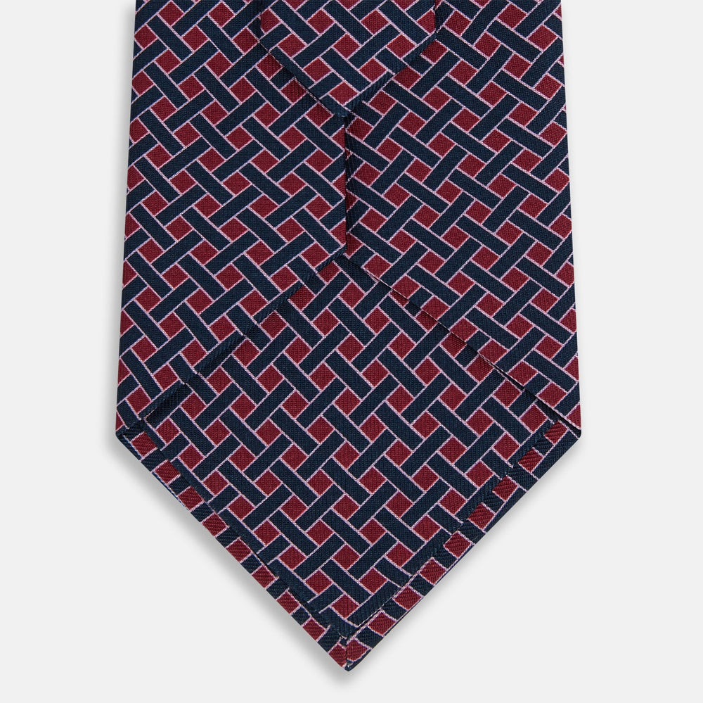 The Turnbull & Asser Navy and Pink Woven Printed Silk Tie features a geometric pattern with interlocking lines, displayed rolled on a light background—perfect for pairing with formal shirts.
