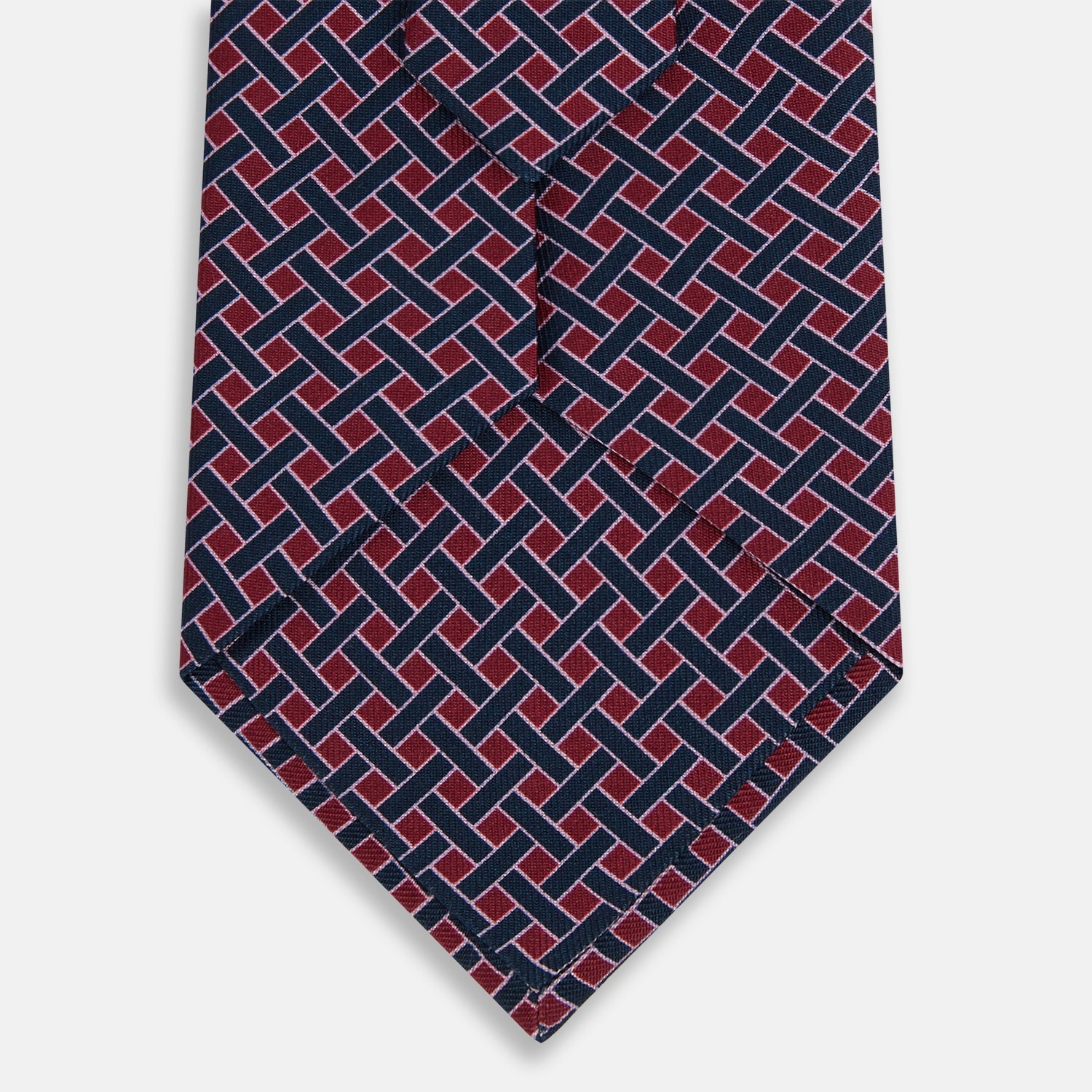 View 3 of product The Turnbull & Asser Navy and Pink Woven Printed Silk Tie features a geometric pattern with interlocking lines, displayed rolled on a light background—perfect for pairing with formal shirts.