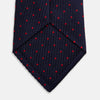 View 4 of product The Turnbull & Asser LACE ON TONE SPOT NAVY TULIP RED TIE is a classic men's accessory crafted from textured navy fabric with small red polka dots, neatly rolled with the pointed end facing forward.
