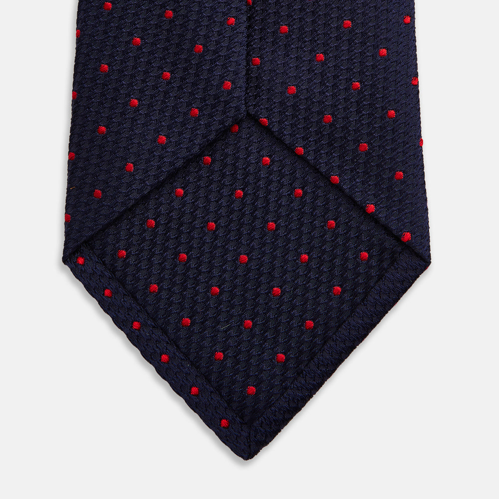 The Turnbull & Asser LACE ON TONE SPOT NAVY TULIP RED TIE is a classic men's accessory crafted from textured navy fabric with small red polka dots, neatly rolled with the pointed end facing forward.