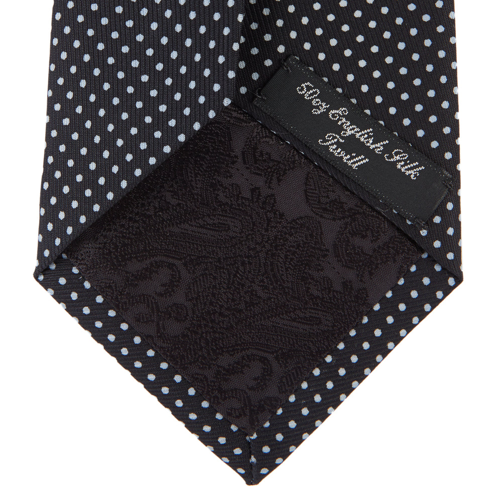 The Turnbull & Asser Black and White Small Spot Printed Silk Tie, shown rolled against a white background, features a subtle polka dot pattern—an ideal accessory for any office shirt.