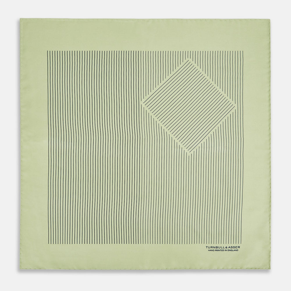 The Melon Green Stripe Silk Pocket Square by Turnbull & Asser features thin vertical black lines on light green silk, neatly folded to display both sides. The lower corner reads “TURNBULL & ASSER HAND PRINTED IN ENGLAND.”.