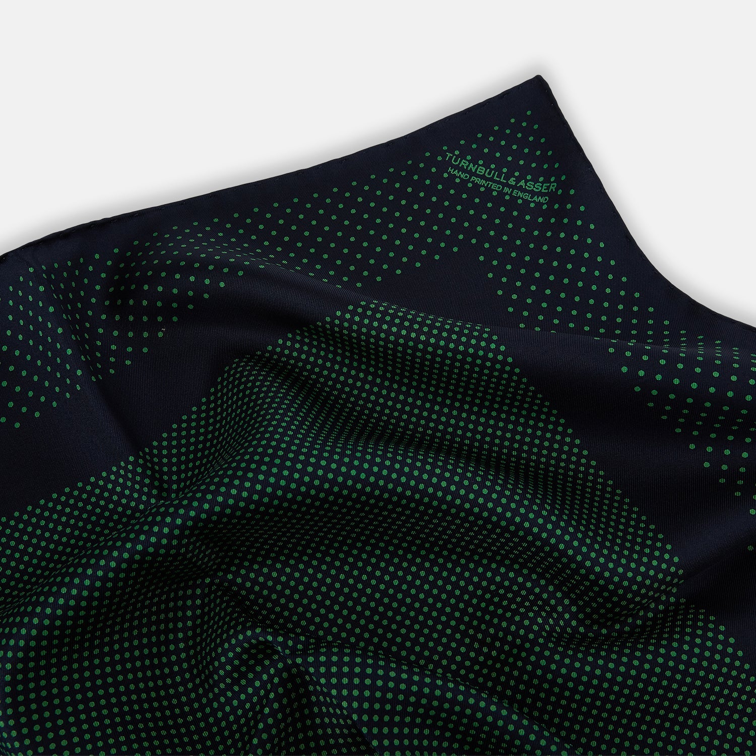 View 2 of product The Turnbull & Asser Navy and Green Dot Silk Pocket Square features dense green polka dots on navy silk, a solid navy border, and a band of spaced green dots—expertly handmade with precise finishing for an elegant look.