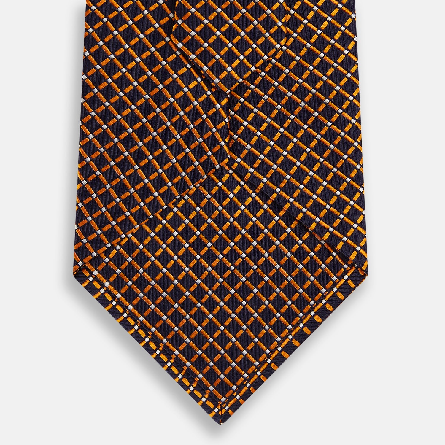 View 3 of product The Turnbull & Asser Orange and Navy Diamond Silk Tie features a yellow and orange diamond pattern on navy silk, ideal for modern office attire, and is displayed rolled up on a light surface.