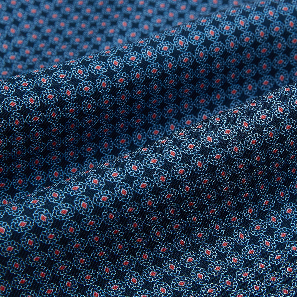 The Turnbull & Asser Navy and Red Rosette Cravat is adorned with a repeating geometric pattern of red, white, and light blue circles—an ideal formal accessory displayed against a white background.