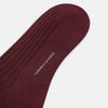 View 3 of product A single Burgundy Long Sock by Turnbull & Asser is shown on a white background, angled to display its over-the-calf length, fitted shape, and ribbed texture along the calf and foot.
