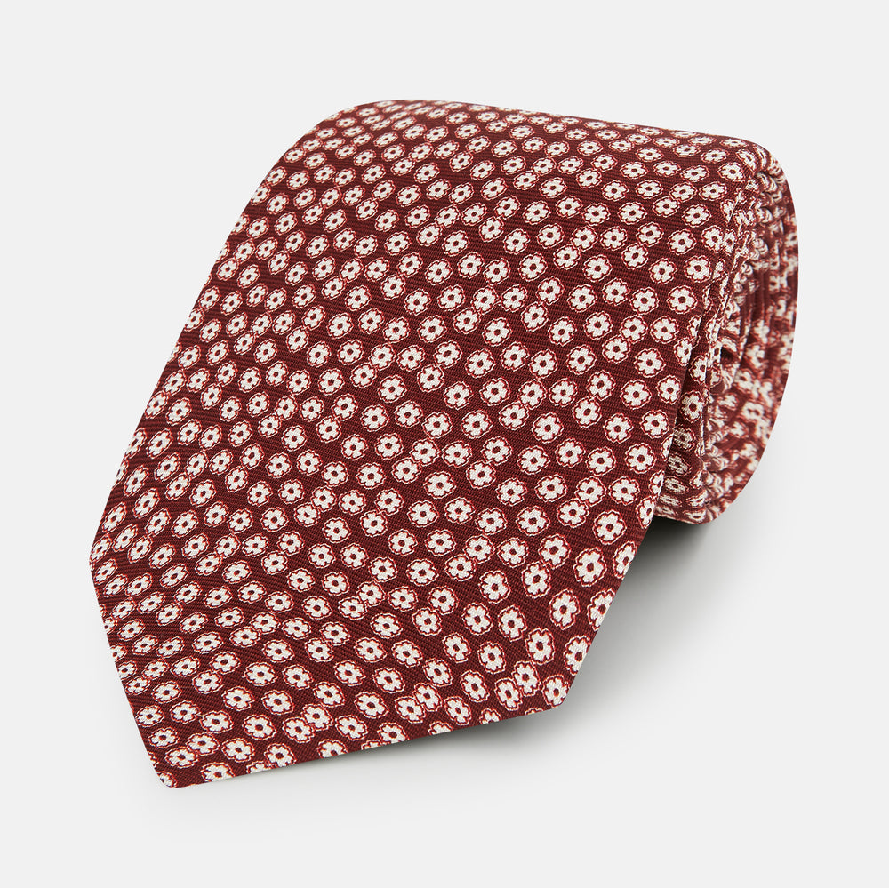 Turnbull & Asser's Burgundy Flower Patterned Silk Tie features small white and light red floral circles, shown rolled on a plain white background.