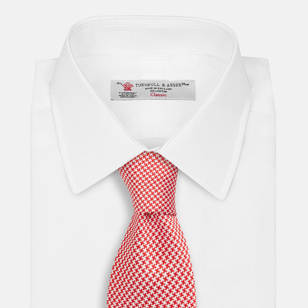 The HOUNDSTOOTH WHITE TULIP RED TIE by Turnbull & Asser features a refined red and white houndstooth pattern—an elegant accessory that elevates any crisp shirt or formal look.