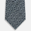 View 3 of product The Turnbull & Asser Navy Flower Patterned Silk Tie is shown rolled up, displaying a repeating floral design with small white and light blue circles on navy, set against a plain white background.