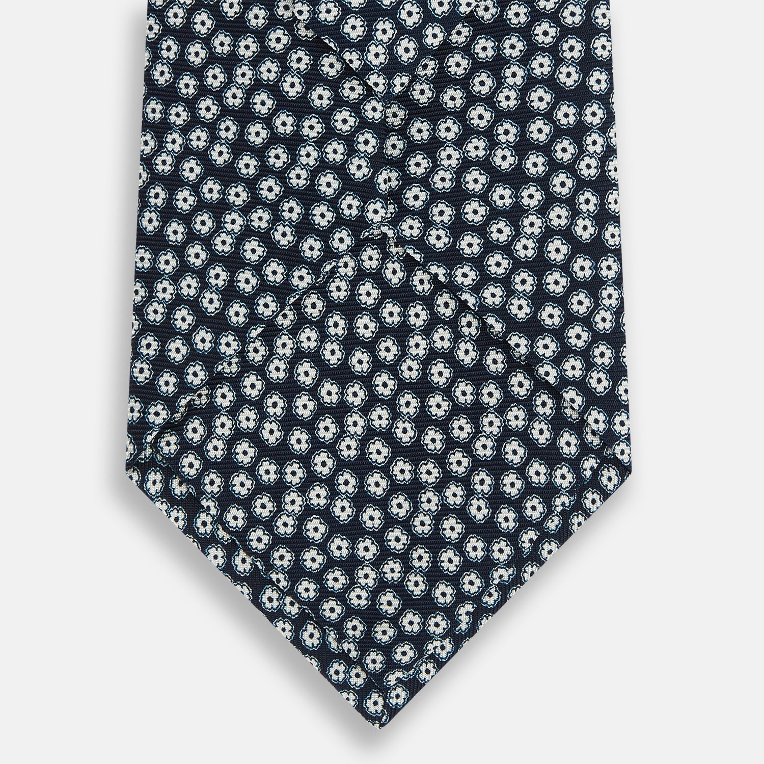 View 3 of product The Turnbull & Asser Navy Flower Patterned Silk Tie is shown rolled up, displaying a repeating floral design with small white and light blue circles on navy, set against a plain white background.