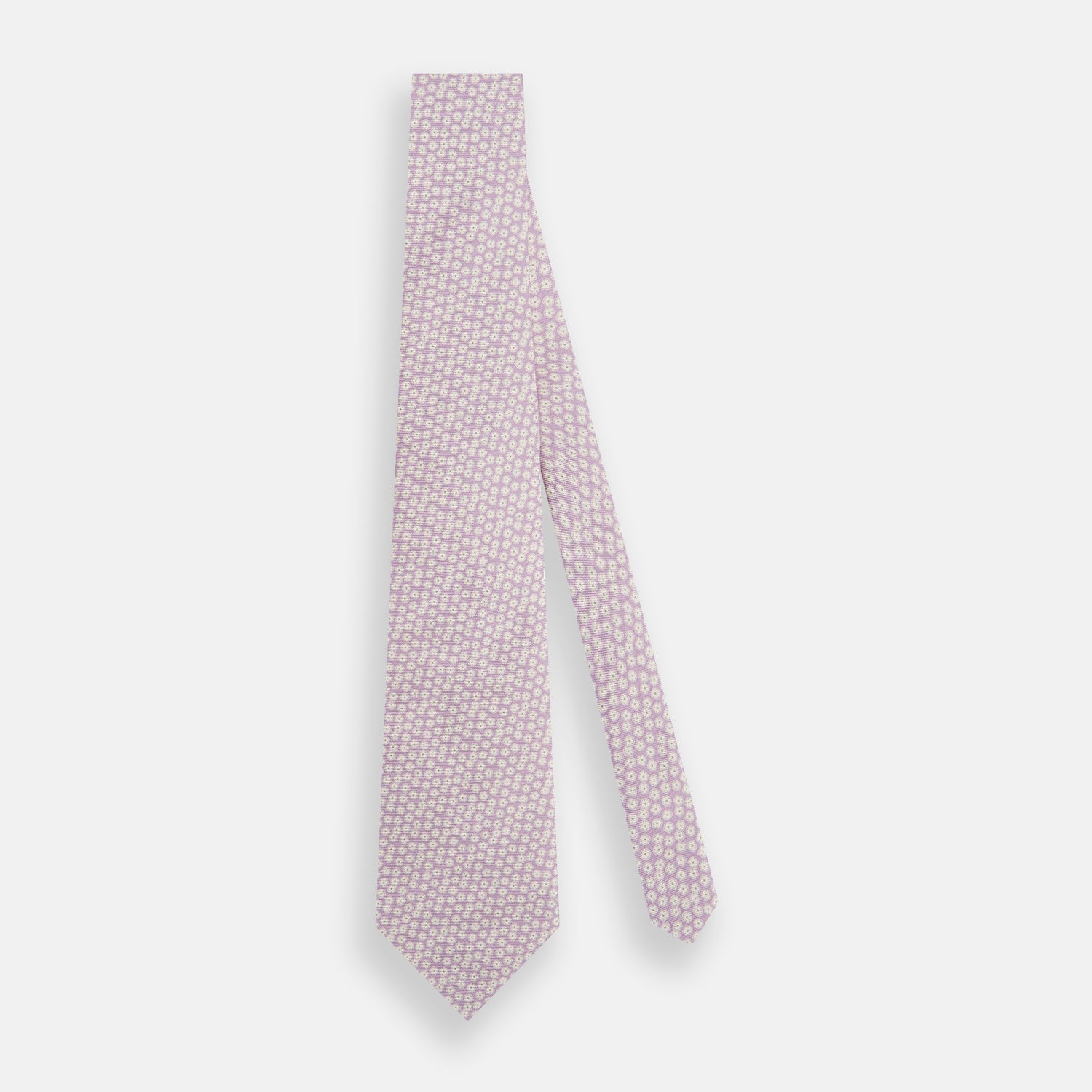 View 2 of product The Turnbull & Asser Lilac Flower Patterned Silk Tie features a light pink hue with a repeating white floral motif, shown rolled up on a plain white background.