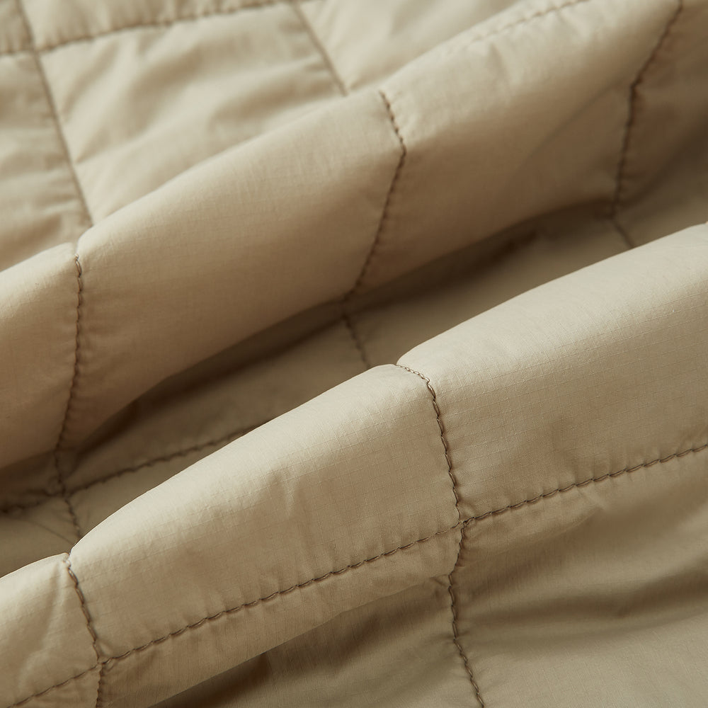 The Turnbull & Asser Sand Quilted Gilet is a beige, lightweight vest featuring a front zipper, two zippered side pockets, a chest pocket, and a rounded hem, shown against a white background.