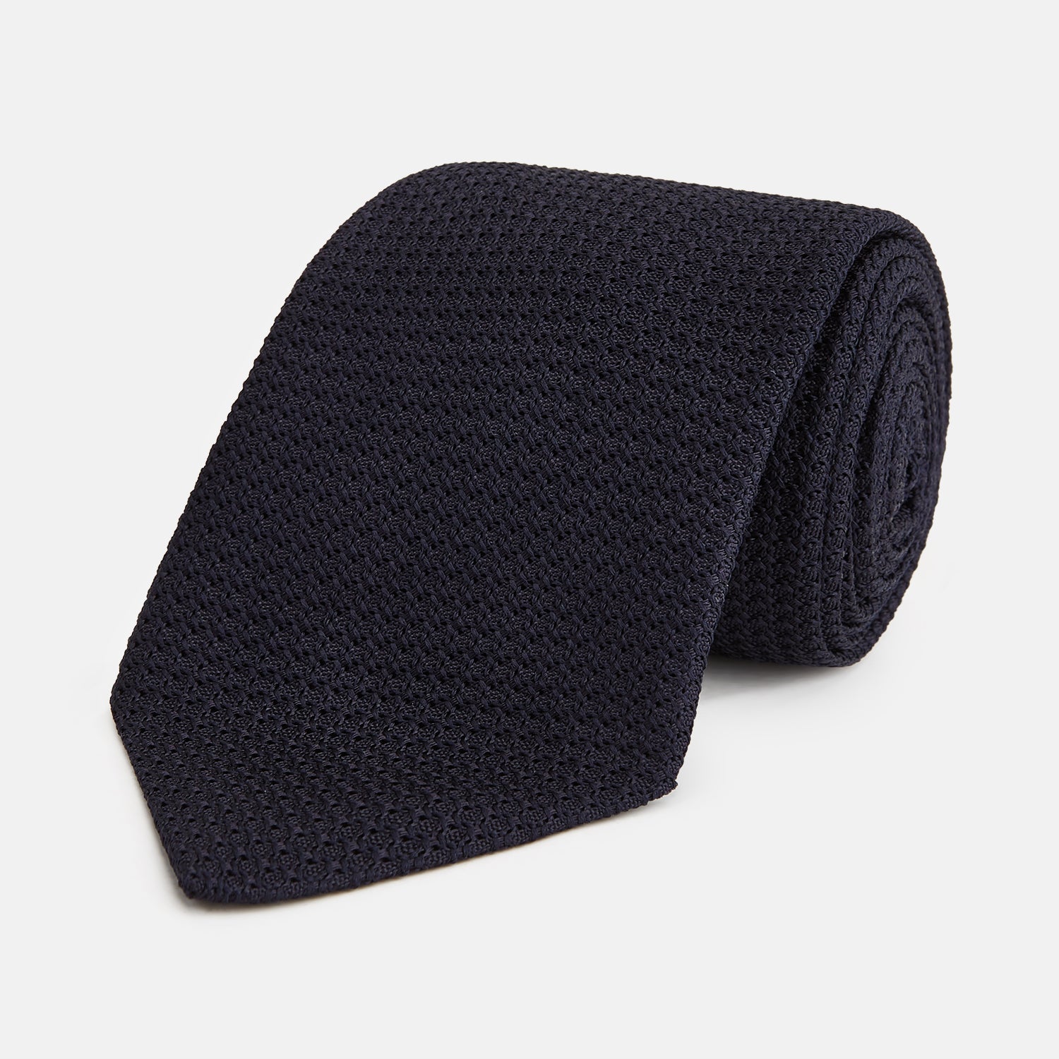View 1 of product The GRENADINE NAVY TIE by Turnbull & Asser—a rolled, dark navy blue textured tie—serves as an essential accessory for smart outfits, shown against a plain white background.