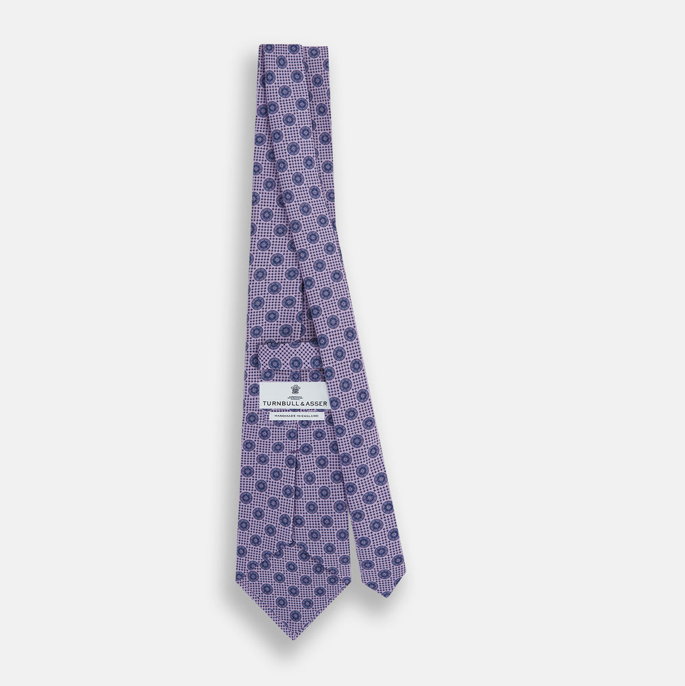 The Turnbull & Asser Lilac Medallion Silk Tie features a repeating navy medallion motif on textured lilac silk, adding refined style to any ensemble.