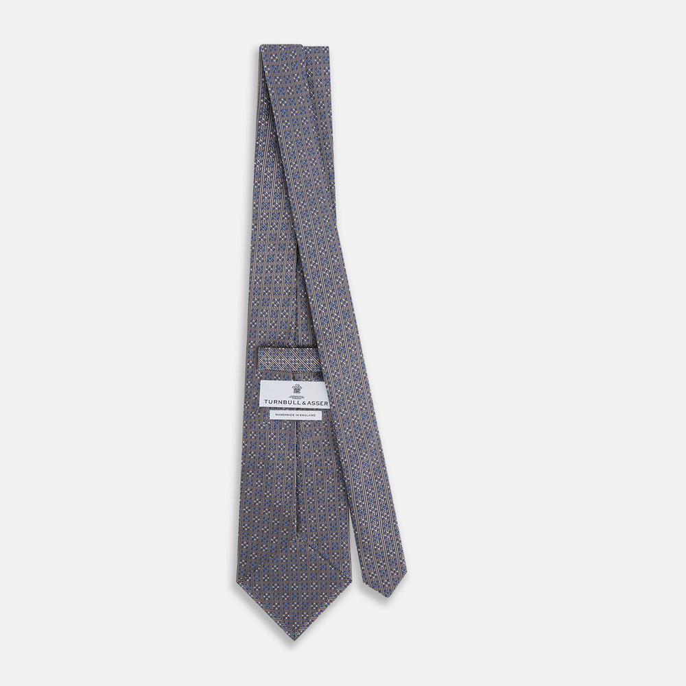 The Turnbull & Asser Silver and Pale Blue Multi Dot Silk Tie features elegant small dots on light brown silk, ideal for modern office wear, shown rolled up against a white background.