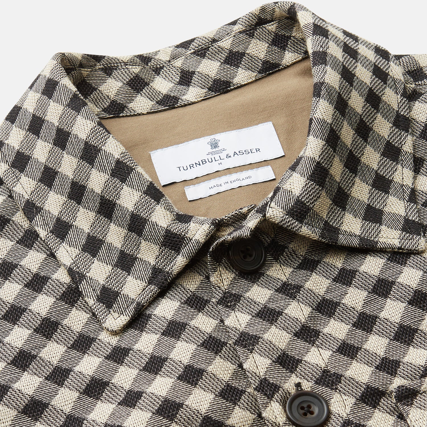 View 2 of product The Turnbull & Asser Black Gingham Check Wool Blend Somerset Overshirt features long sleeves, two chest flap pockets with buttons, and a black-and-beige check pattern. Shown laid flat on a white background; ideal as transitional outerwear.