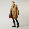 View 3 of product A person wears the Turnbull & Asser Camel Quintern Sealup Raincoat with Detachable Liner, paired with dark pants, standing against a plain light gray background, showing the sleek technical rainwear style with one hand in a pocket.