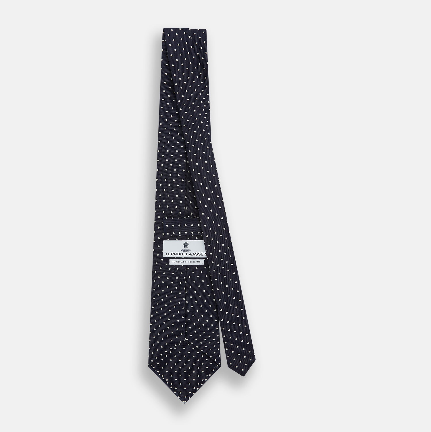 View 4 of product The Silver and Navy Micro Dot Silk Tie by Turnbull & Asser features a refined micro dot pattern, perfect for adding a classic accent to formal attire. Shown neatly rolled on a white background.