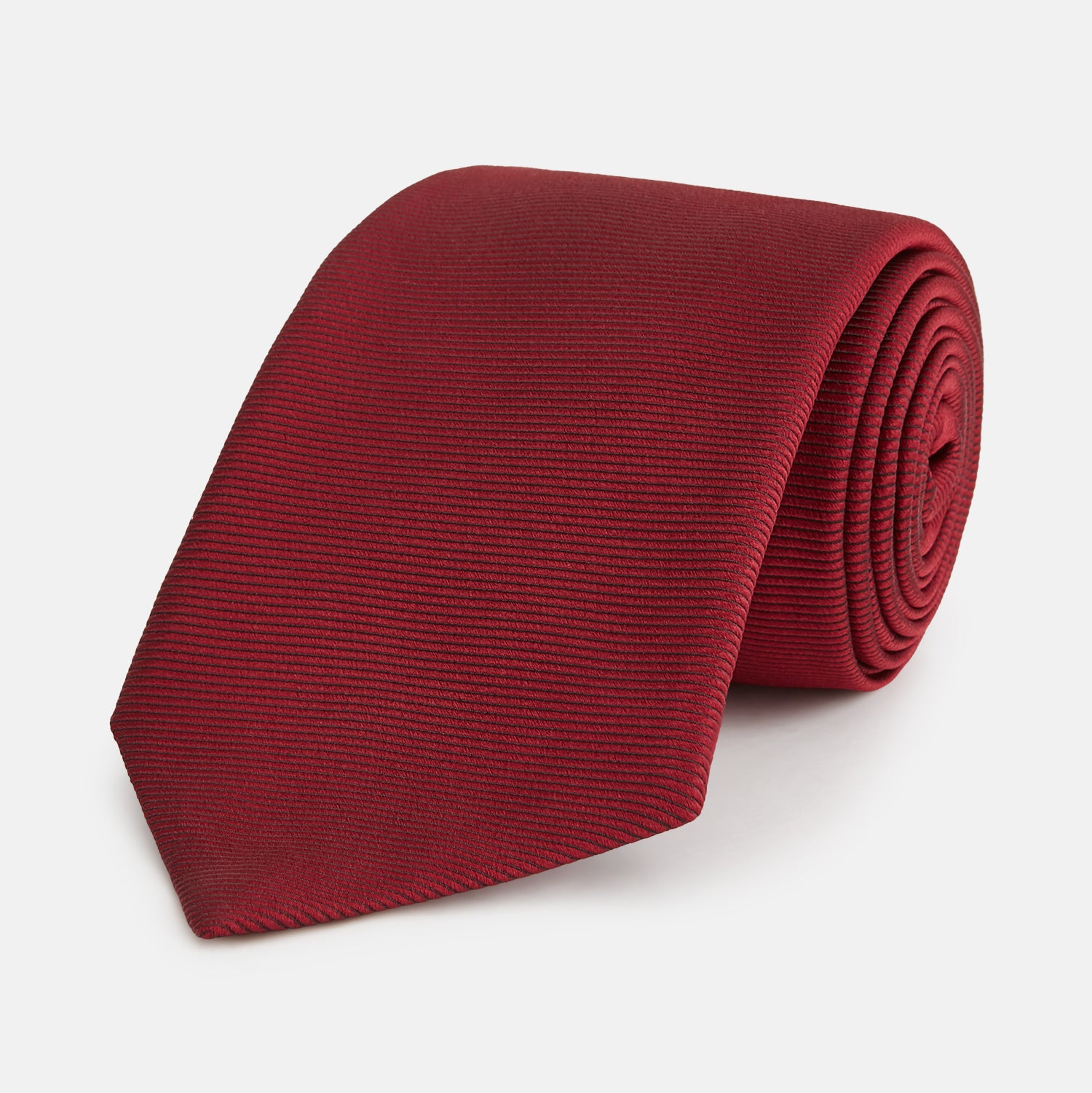 View 1 of product The HORIZONTAL TWILL BURGUNDY TIE by Turnbull & Asser features a subtle textured pattern in solid burgundy, rolled neatly and displayed against a white background—a versatile addition to any gentleman’s wardrobe.