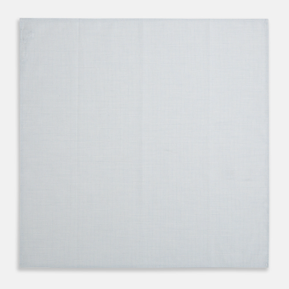 The Turnbull & Asser Hand Rolled Pale Blue Graph Check Handkerchief features a neatly folded white cotton design with a pale blue check, offering an elegant finishing touch to any setting.