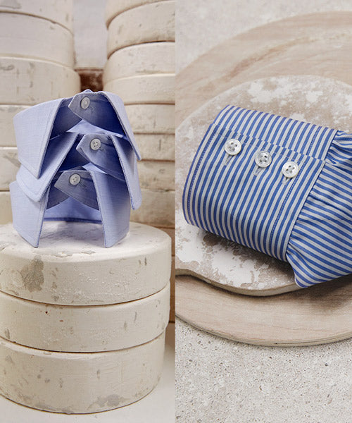 Two blue dress shirts stacked creatively on white circular stone slabs, alongside a blue-and-white striped shirt sleeve neatly laid on a round stone platter.