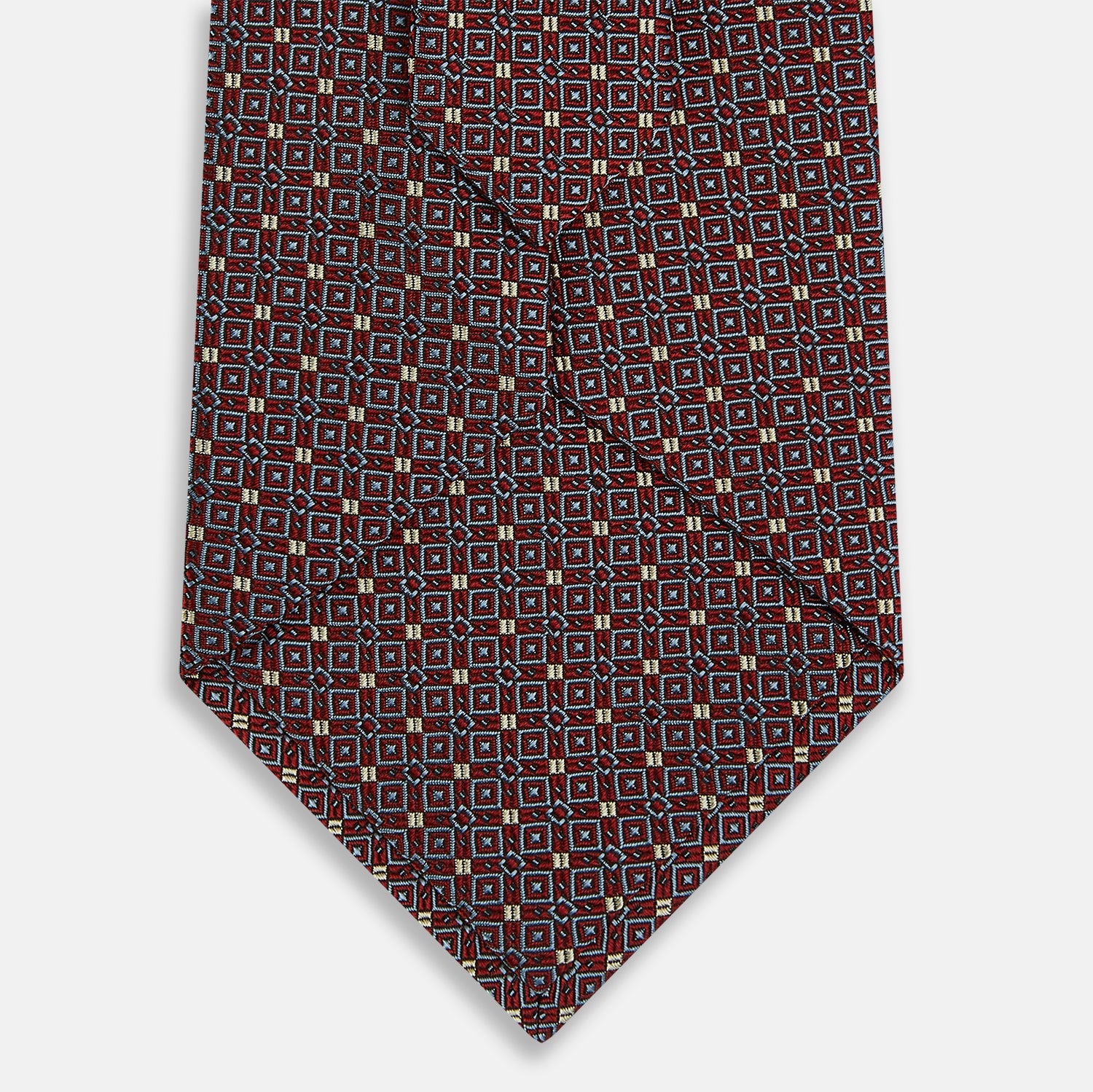 View 3 of product The Turnbull & Asser Burgundy Geometric Silk Tie, crafted in Britain, features a repeating pattern of light blue and white squares and diamonds. The neatly rolled tie is shown against a plain white background.